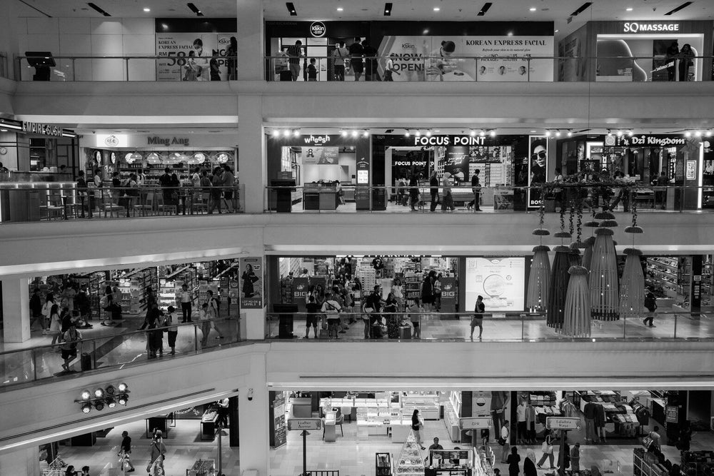 fotografie alb-negru cu etaje de mall pline de oameni, reprezentând societatea de consum